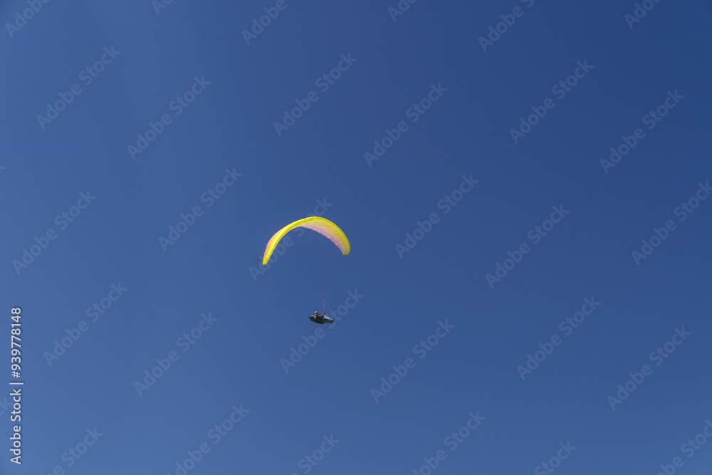 Paraglider soaring high in the sky with a yellow canopy, under a bright sun and scattered clouds. Paraglider soaring high in the sky with a yellow canopy, under a bright sun and scattered clouds.