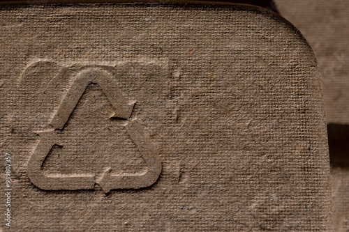Recycling Symbol on Cardboard Texture. Close-up of a recycling symbol embossed on a rough cardboard surface, emphasizing eco-friendly packaging and sustainability.

