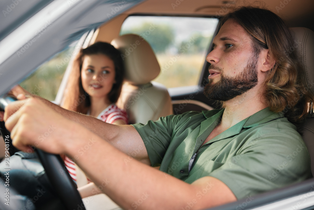 Young couple in a car enjoying a road trip on a sunny day, with the driver focused and the passenger smiling, creating a lively atmosphere Young couple in a car enjoying a road trip on a sunny day, with the driver focused and the passenger smiling, creating a lively atmosphere
