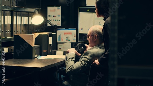 Paralyzed senior inspector reviewing classified case records in incident room, gathering intelligence for private investigation. Wheelchair user with limited mobility accessing databases. Camera A.