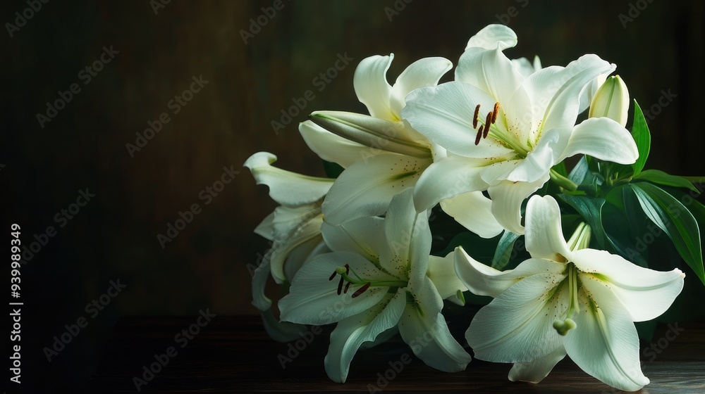 Fototapeta premium A bouquet of white lilies placed on a dark wooden table, with soft light highlighting their petals