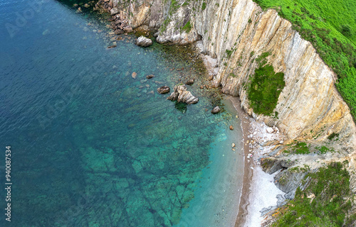 Aerial view of a secluded beach with clear turquoise water, rocky shoreline, and steep cliffs covered in greenery