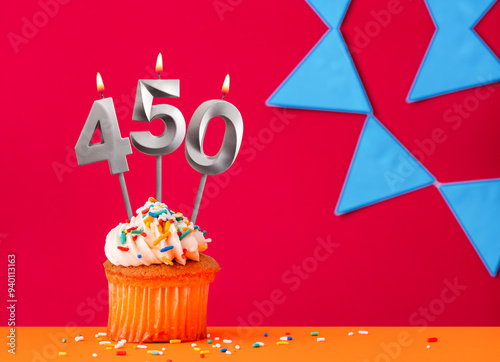 Number 450 candle with birthday cupcake on a red background with blue pennants