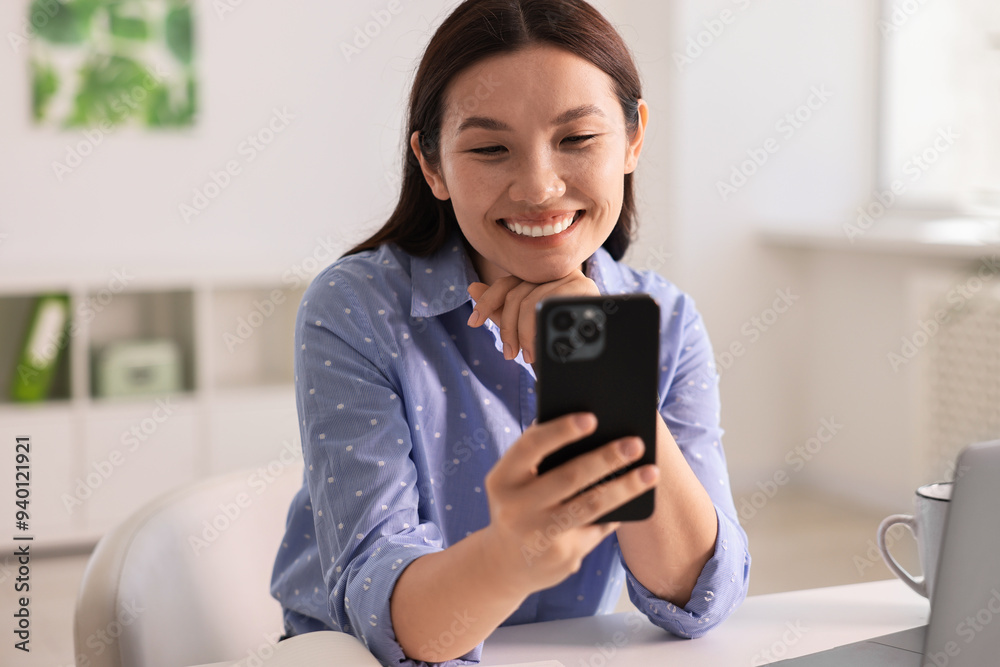 Smiling businesswoman with smartphone at table in office Smiling businesswoman with smartphone at table in office