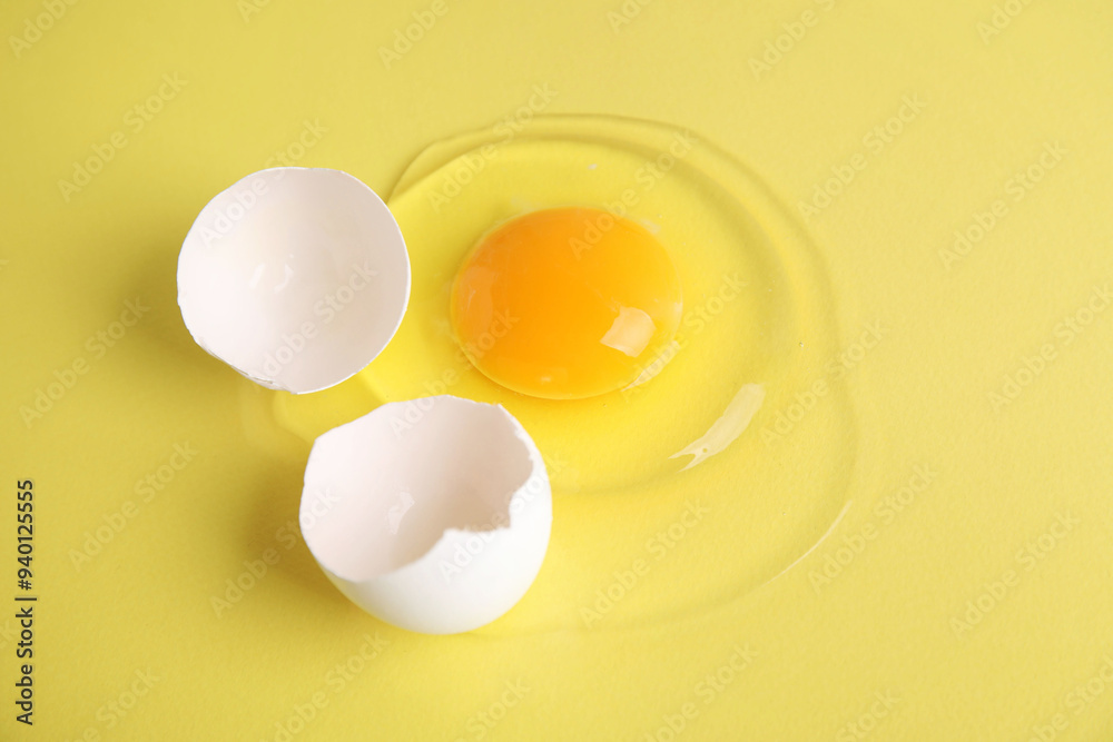 Broken raw egg and shell on yellow background, closeup Broken raw egg and shell on yellow background, closeup