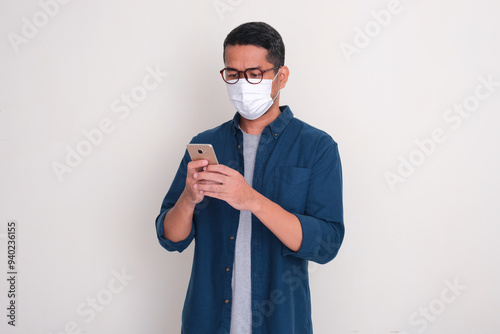 A man wearing medical face mask typing something on his mobile phone photo