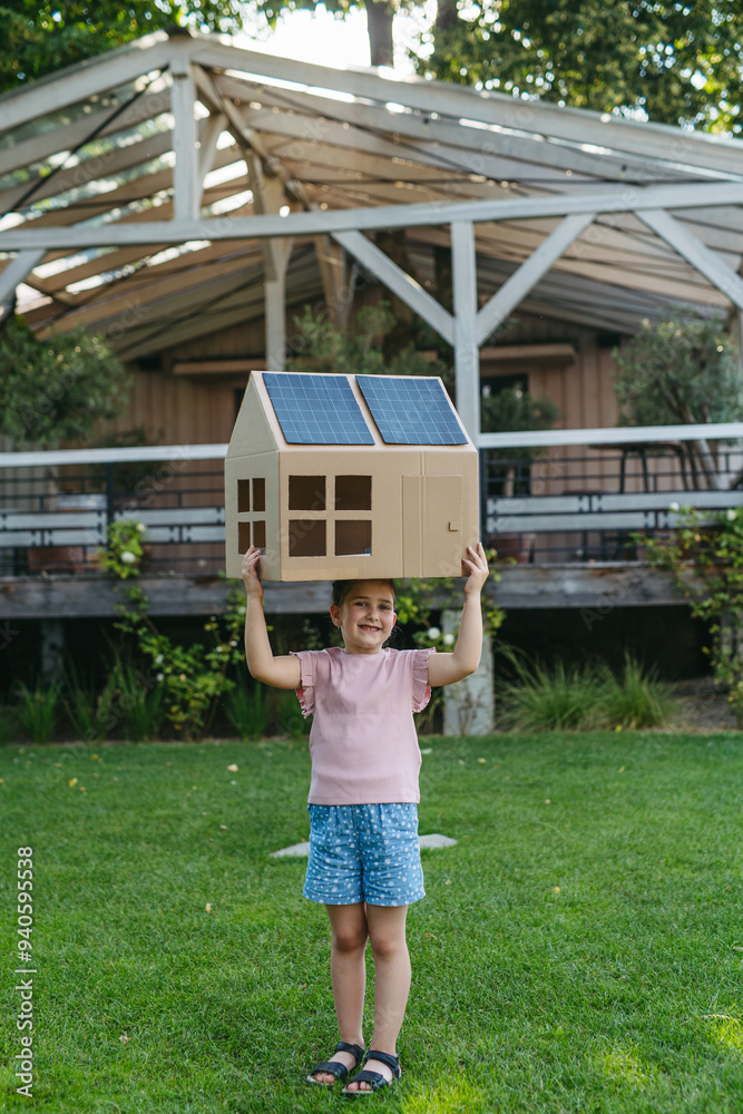 Fototapeta premium Girl holding house with solar panels on roof, learning about solar energy. Rooftop solar or photovoltaic system. Sustainable future for next generation.