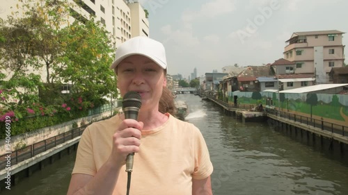 Reporter with microphone is broadcasting on street of Old Bangkok. Female correspondent is reporting.
