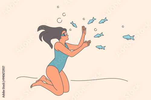 Woman diver swims underwater among fish, holding breath without using scuba gear and mask