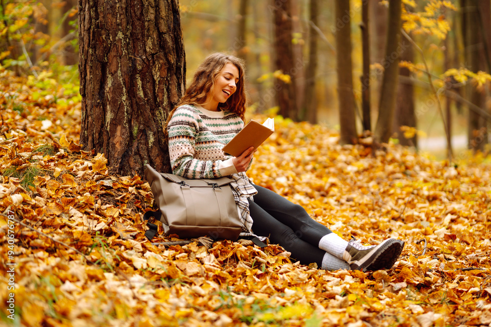 A young woman enjoys a quiet moment, immersed in a book while seated on colorful fallen leaves. . Education. Concept of enjoying nature. A young woman enjoys a quiet moment, immersed in a book while seated on colorful fallen leaves. . Education. Concept of enjoying nature.