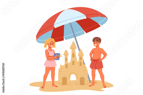 Children build sand castle on beach, standing with umbrella to protect them from sun. Little positive boy and girl play together on beach during summer trip to sea or ocean with parents