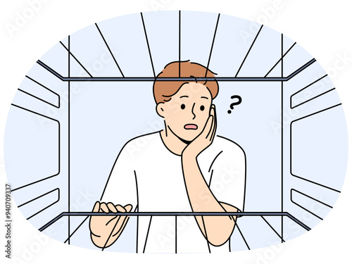 Hungry man sees empty refrigerator and is nervous about lack food due to poverty and financial crisis. Young embarrassed guy looks into refrigerator compartment surprised by lack products on shelves