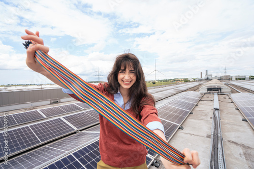 Smiling businesswoman holding multi colored wire strap and standing on rooftop with solar panels photo