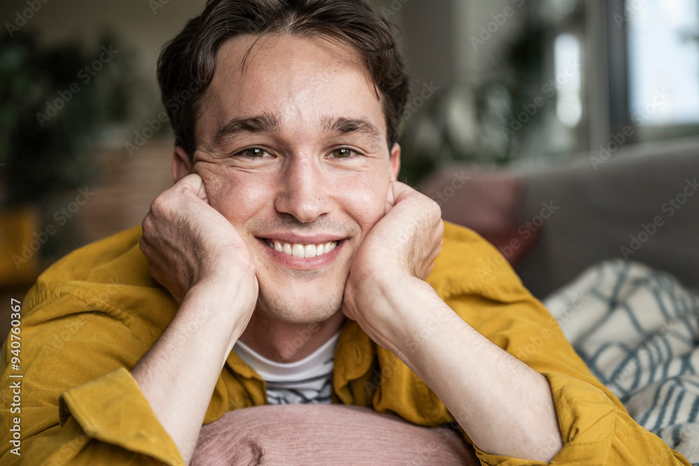 Smiling young man leaning on elbows and lying down on sofa at home Smiling young man leaning on elbows and lying down on sofa at home