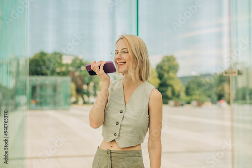 Happy woman talking through speaker phone near glass wall