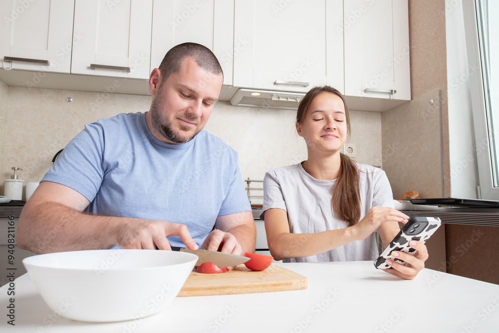 Teenage girl and father cook using a recipe on phone, parent and teenager in the kitchen, enjoying the fun and happiness of meal preparation. Teenage girl and father cook using a recipe on phone, parent and teenager in the kitchen, enjoying the fun and happiness of meal preparation.