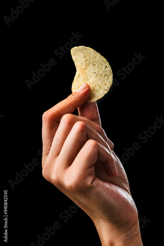 holding a single potato chip held between fingers, isolated on black background