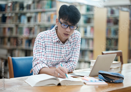 Young Asian male sitting inside a library alone doing research. Man working on a project. Young man doing research for a case.