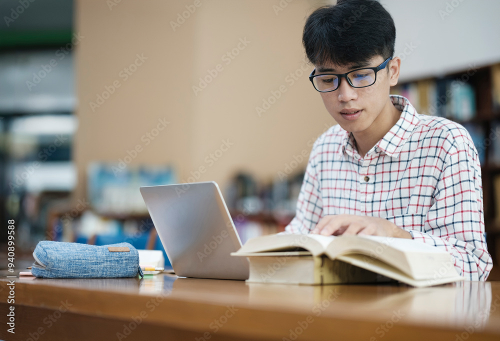 Young Asian male sitting inside a library alone doing research. Man working on a project. Young man doing research for a case. Young Asian male sitting inside a library alone doing research. Man working on a project. Young man doing research for a case.