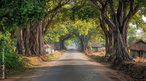 A peaceful rural road in the Indian countryside, lined with banyan trees and small huts along the way