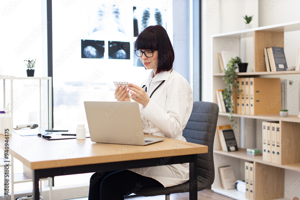 Female doctor in office sitting at desk reviewing medication. Medical professional analyzing pills with laptop and medical documents. Bright, modern workspace promoting healthcare and precision. Female doctor in office sitting at desk reviewing medication. Medical professional analyzing pills with laptop and medical documents. Bright, modern workspace promoting healthcare and precision.