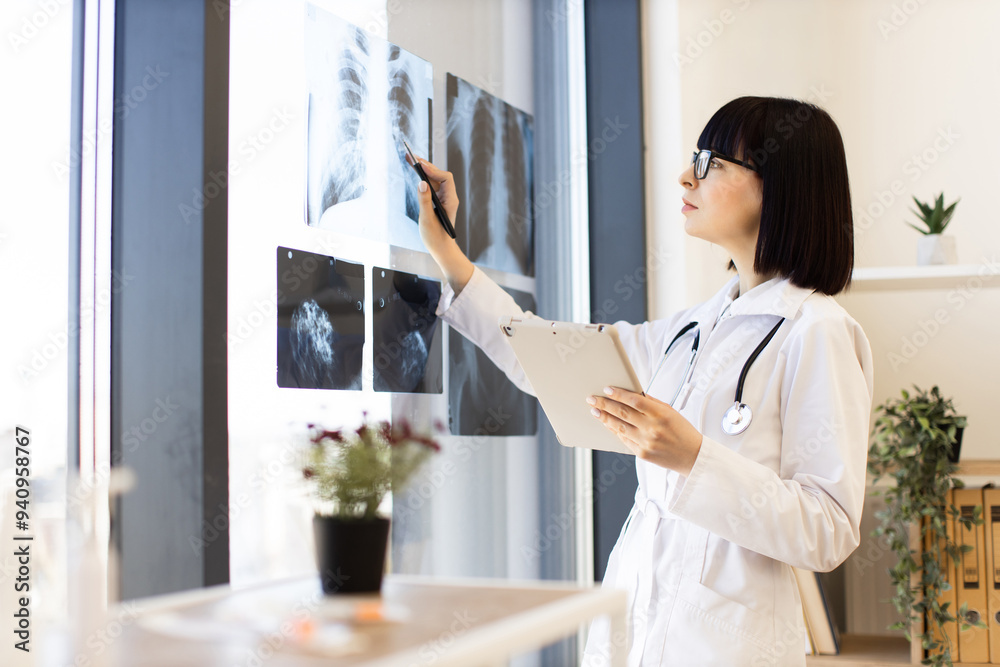 Female doctor studying X-rays using tablet in bright modern medical office. Professional healthcare worker in clinical environment focusing on patient diagnosis Female doctor studying X-rays using tablet in bright modern medical office. Professional healthcare worker in clinical environment focusing on patient diagnosis