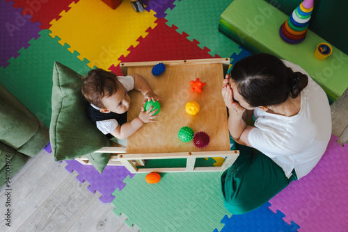 Concentrated boy during SIT classes with educational psychologist holding colored ball for development of sensory sensitivities, top view. Sensory integration therapy
