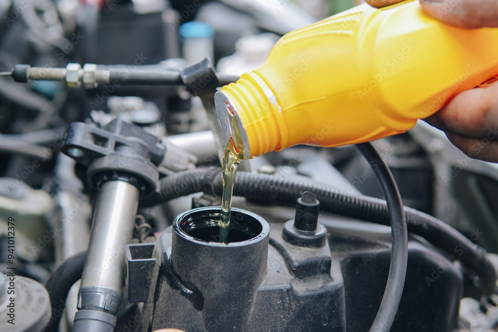 Fototapeta premium A man is pouring oil into a car engine
