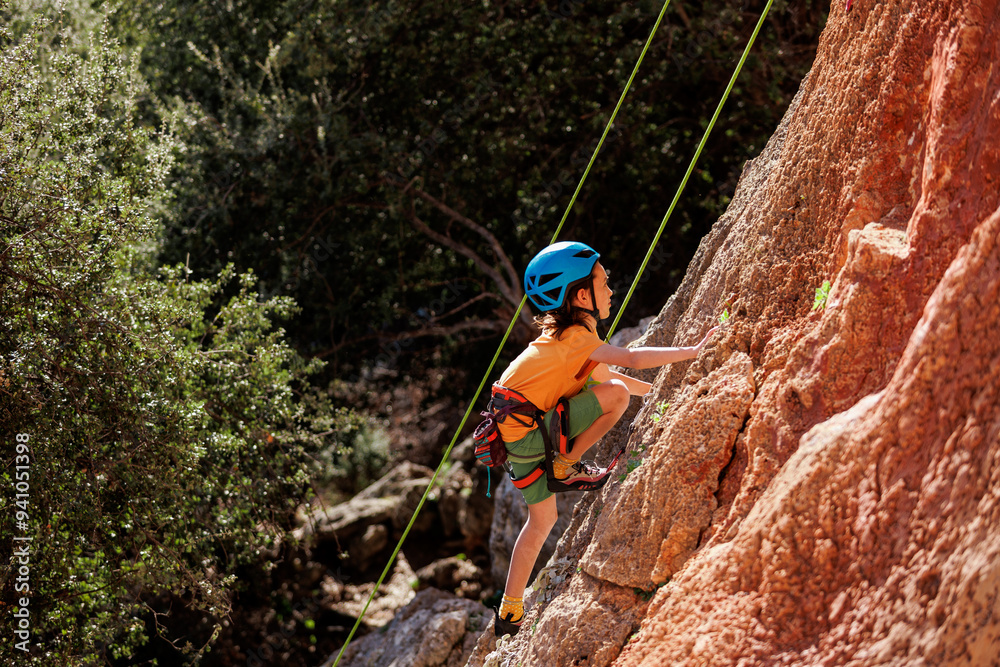 Obraz premium child is rock climbing at a summer camp. rock climber boy. sport in nature. cute teenager climbs a rock with a belay. active holidays.