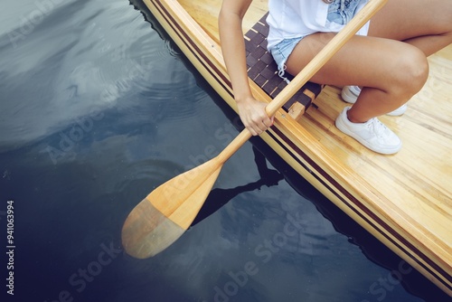 Person paddling a wooden canoe on calm blue water.