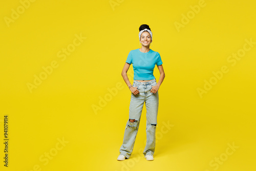 Full body young smiling happy cheerful fun cool Latin woman she wearing blue top t-shirt headband casual clothes standing looking camera isolated on plain yellow background studio. Lifestyle concept.