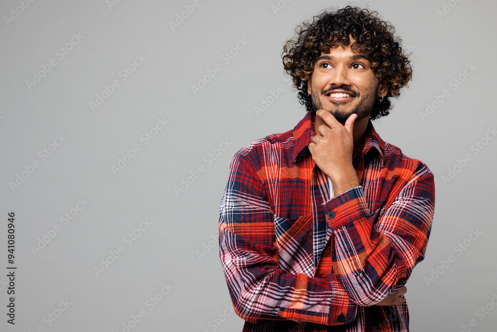 Φωτογραφία Young happy smiling Indian man he wears red shirt casual clothes put hand prop up on chin, lost in thought and conjectures isolated on plain grey color background studio portrait