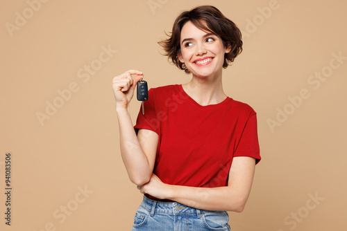 Fotografía Young smiling happy woman wear red t-shirt casual clothes hold in hand car key fob keyless system look aside on area isolated on plain pastel light beige background studio portrait