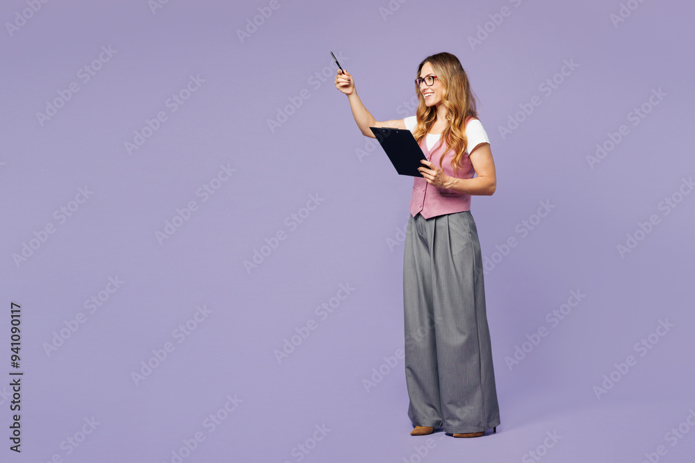 Full body young employee business woman corporate lawyer wearing classic suit vest white t-shirt work in office hold clipboard paper account documents point aside isolated on plain purple background. Full body young employee business woman corporate lawyer wearing classic suit vest white t-shirt work in office hold clipboard paper account documents point aside isolated on plain purple background.