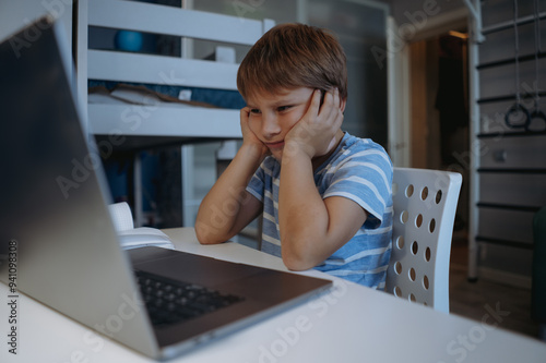 cute little boy studying at home usung laptop, tired, sressed, thinking hard trying to do homework photo