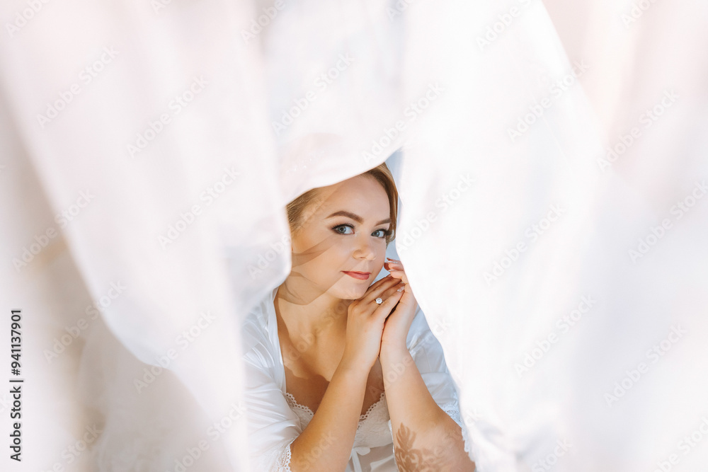 A woman is sitting in a room with a white curtain behind her. She is wearing a white dress and has her hands on her knees. The room is dimly lit, and the woman is in a contemplative mood A woman is sitting in a room with a white curtain behind her. She is wearing a white dress and has her hands on her knees. The room is dimly lit, and the woman is in a contemplative mood