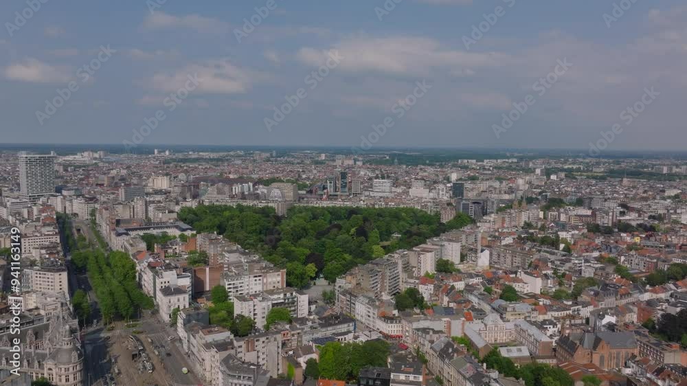 Camera pans over a vast cityscape, showcasing the urban sprawl of Antwerp, Belgium. The focus shifts to a lush green park, providing a stark contrast to the surrounding concrete jungle Camera pans over a vast cityscape, showcasing the urban sprawl of Antwerp, Belgium. The focus shifts to a lush green park, providing a stark contrast to the surrounding concrete jungle