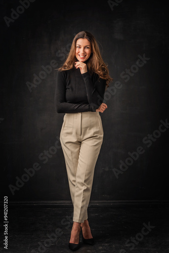 Full length of a brunette haired woman toothy smiling and standing with arms crossed at isolated dark background