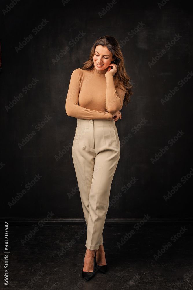 Full length of a brunette haired woman toothy smiling and standing with arms crossed at isolated dark background Full length of a brunette haired woman toothy smiling and standing with arms crossed at isolated dark background