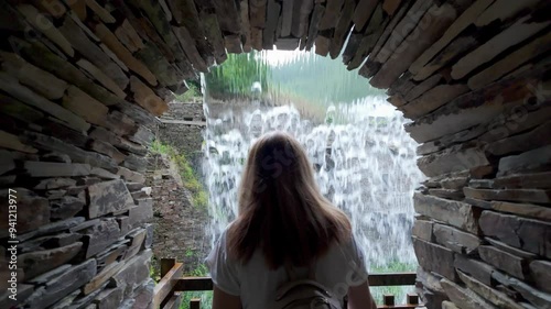 Tourist woman passing through a stone tunnel that flows into a large waterfall of river water, Taramundi, Asturias.