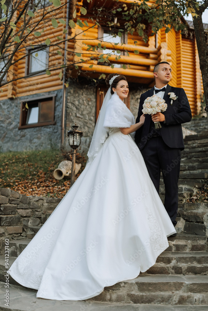 Fototapeta premium A bride and groom are standing on a set of stairs in front of a log cabin