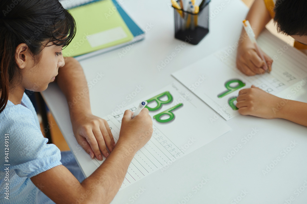 Two children practicing handwriting skills in classroom, focusing on formation of letters while writing on worksheets, emphasizing attention to detail and collaboration Two children practicing handwriting skills in classroom, focusing on formation of letters while writing on worksheets, emphasizing attention to detail and collaboration