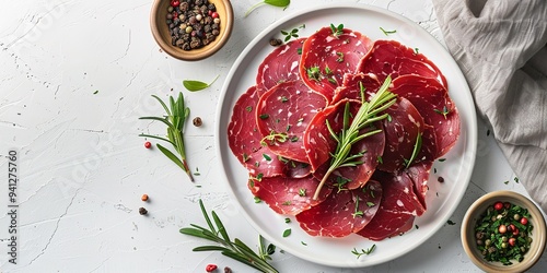 A spotless white dish with dried beef bresaola slices and herbs is shown from above and up against a spotless white background in a studio, Generative AI.