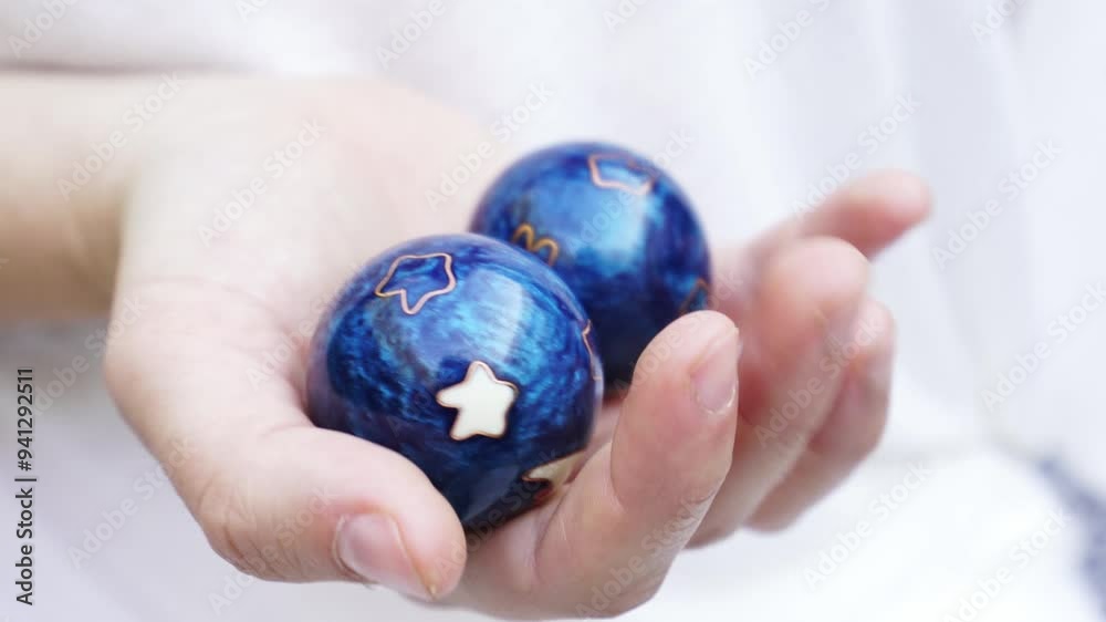 A hand holding two blue balls with a sun on one of them A hand holding two blue balls with a sun on one of them
