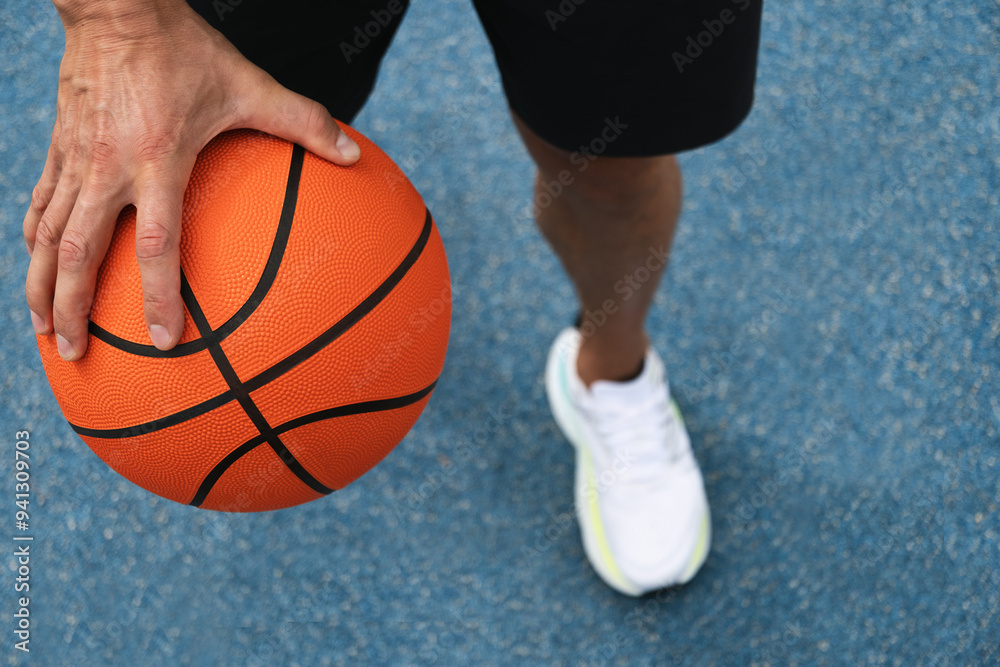 Basketball orange ball in man hand on blue court. Sport background. Team sport. Close up. Basketball orange ball in man hand on blue court. Sport background. Team sport. Close up.