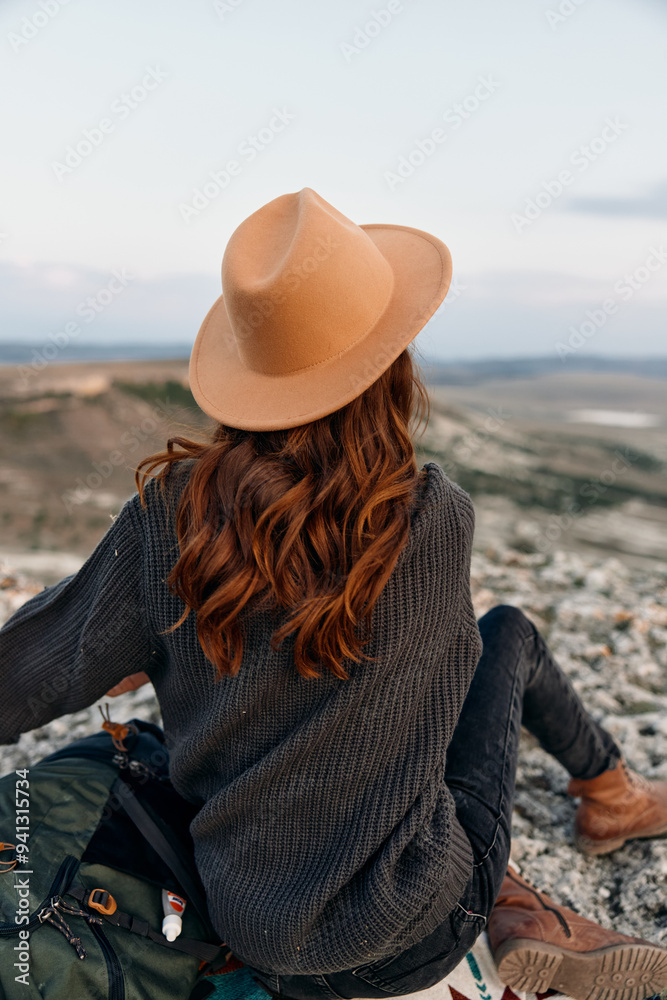 adventurous woman in hat and backpack sitting on mountain peak, enjoying the stunning view adventurous woman in hat and backpack sitting on mountain peak, enjoying the stunning view