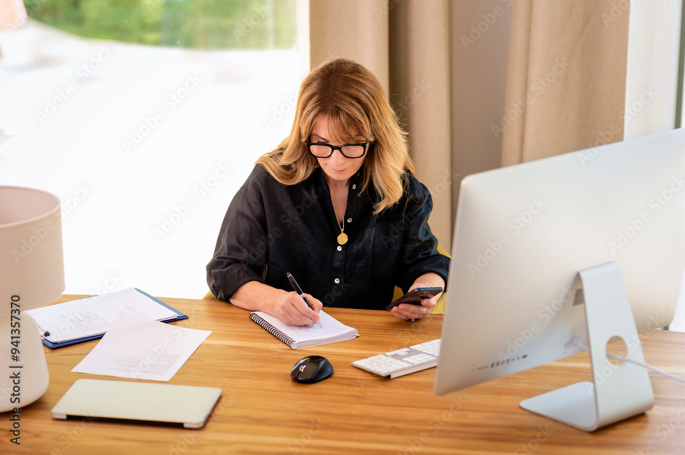 Confident businesswoman sitting at desk and using a smarphone and computer for work Confident businesswoman sitting at desk and using a smarphone and computer for work