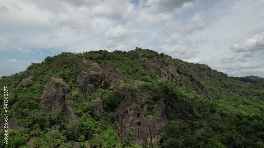 rock formations in the ancient Nglanggeran volcano that were formed millions of years ago. overgrown by green trees typical of the tropics. High ancient black stone towering.