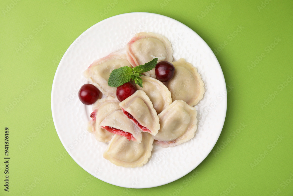 Traditional Ukrainian dumplings (varenyky) with cherries on green background, top view Traditional Ukrainian dumplings (varenyky) with cherries on green background, top view