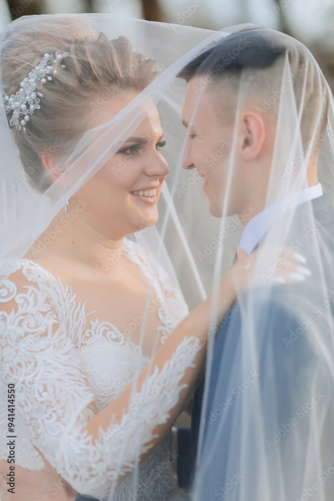 A bride and groom are embracing each other under a veil. The bride is wearing a white dress and the groom is wearing a blue suit. Scene is happy and romantic A bride and groom are embracing each other under a veil. The bride is wearing a white dress and the groom is wearing a blue suit. Scene is happy and romantic